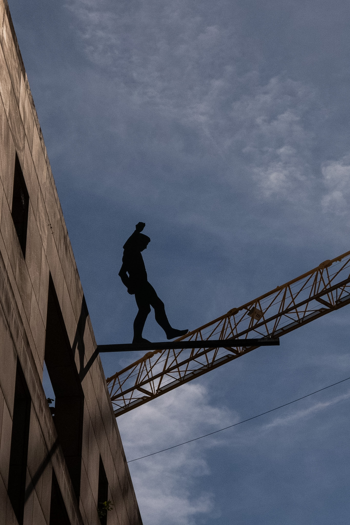Silhouetted figure on a beam with a construction crane against the blue sky
